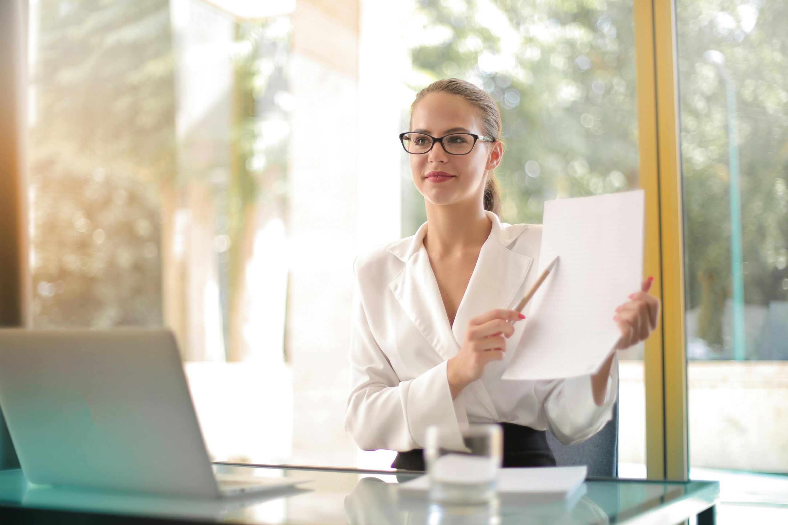 Smart businesswoman in formal attire holding a document in a modern office setting.